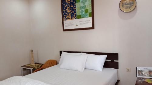 Homestay Suryati Tanjong Tinggi في Pasarbaru: غرفة نوم بسرير من الشراشف البيضاء وساعة على الحائط