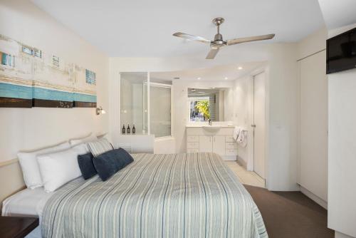 a white bedroom with a bed and a bathroom at French Quarter Apartment 116, Noosa Heads in Noosa Heads