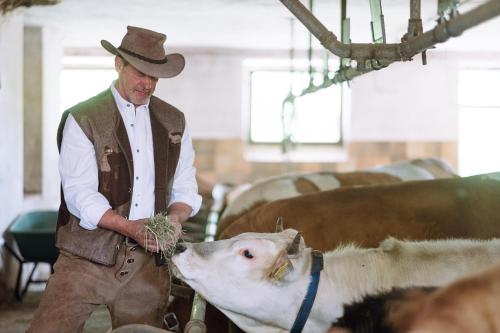 a man in a hat is petting a cow at Naturhotel Miraval in Perca