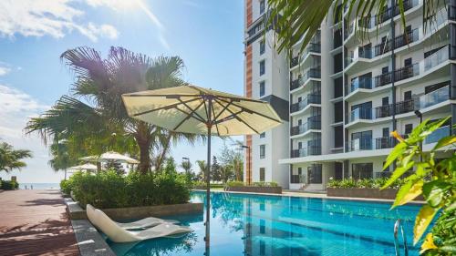 a swimming pool with an umbrella next to a building at Timurbay Seafront Residences by Nature Home in Kuantan
