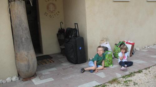 two children sitting next to a building with luggage at BioAgriturismo Vegan Campo di Cielo in Cesiomaggiore