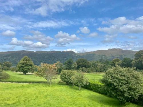 a green field with trees and mountains in the background at Woodlands House with Hot Tub in Ballachulish