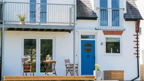 a white house with a blue door and chairs at Noddfa in Menai Bridge