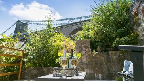 a table with wine glasses and a bridge in the background at Noddfa in Menai Bridge