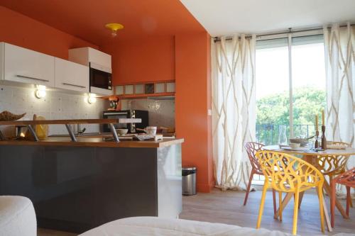 een keuken met oranje muren en een tafel en stoelen bij Studio terrasse Parking CLIM sans vis à vis in La Grande-Motte