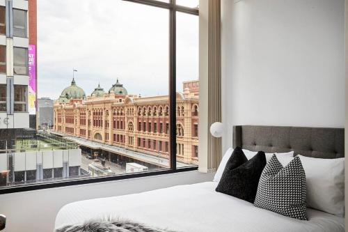 a bedroom with a large window overlooking a large building at Found at Flinders - An Iconic City Stay in Melbourne