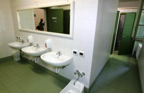 Baño con 3 lavabos, orinal y espejo en Student's Hostel Della Ghiara, en Reggio Emilia