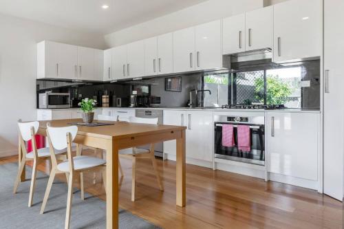 a kitchen with white cabinets and a wooden table and chairs at Trendy and Spacious Brunswick Stay with Outdoor Deck in Melbourne