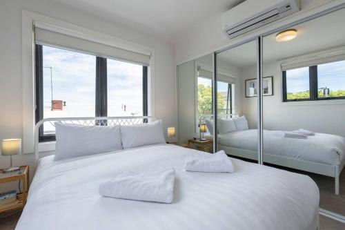a white bedroom with two beds and large windows at Trendy and Spacious Brunswick Stay with Outdoor Deck in Melbourne