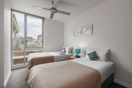 two beds in a room with a large window at Easy Eastside - A Sunny Rooftop Pool Oasis in Melbourne