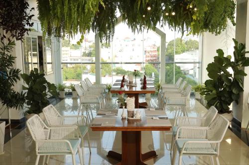 a dining room with white chairs and tables and plants at Pleiku & Em Hotel by Gia Lai Tourist in Pleiku