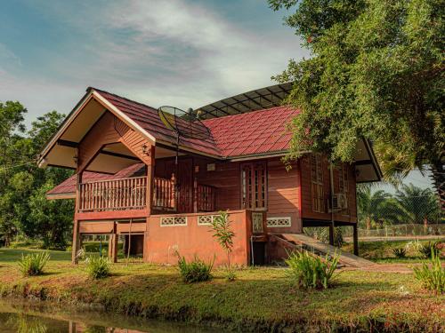 Bakkahland Farm and Resort في Pattani: منزل خشبي بسقف احمر بجانب نهر