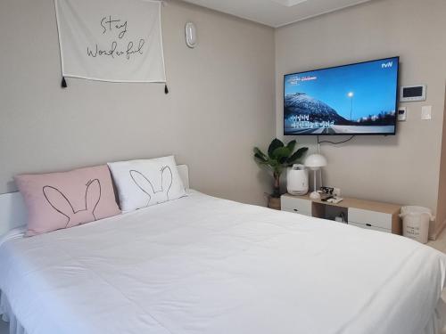 um quarto com uma cama branca e uma televisão de ecrã plano em Yolo House em Daegu