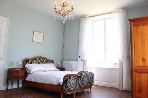 1 dormitorio con cama y lámpara de araña en La Belle Maison, en Eymoutiers