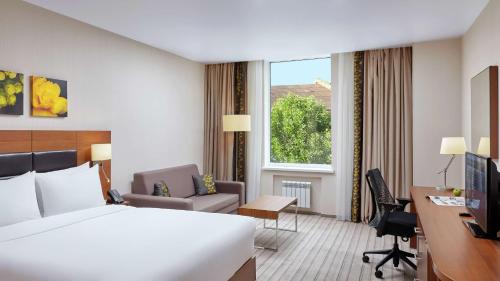 a hotel room with a bed and a desk and a window at Hilton Garden Inn Kaluga in Kaluga