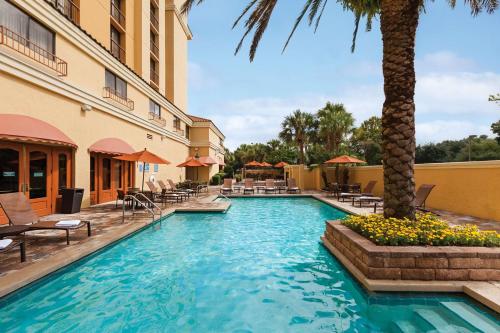 a swimming pool in a hotel with chairs and a palm tree at Embassy Suites by Hilton Orlando International Drive Convention Center in Orlando