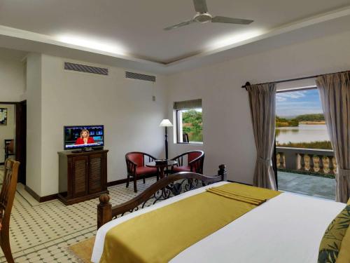 a bedroom with a bed and a television and a balcony at Mercure Goa Devaaya Resort in Old Goa