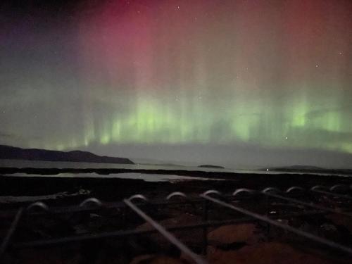 an aurora in the sky over a body of water at Carnmhor, Isle of Skye - Stunning 242 year old cottage on its own sea shore! in Breakish