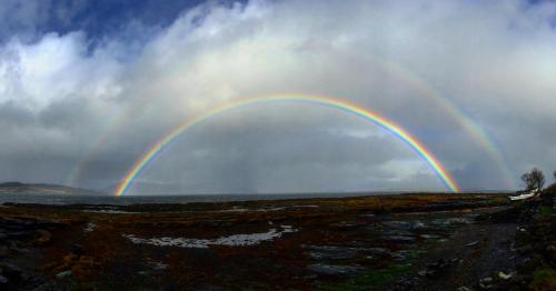a double rainbow in a cloudy sky over a field at Carnmhor, Isle of Skye - Stunning 242 year old cottage on its own sea shore! in Breakish