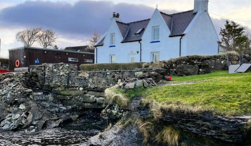 a house with a stone wall next to a river at Carnmhor, Isle of Skye - Stunning 242 year old cottage on its own sea shore! in Breakish