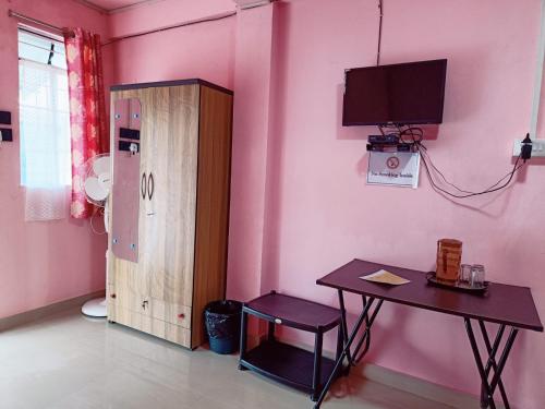 a pink room with a table and a tv on the wall at StayHome Away from Home in Cherrapunji