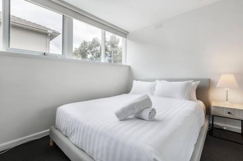 Dormitorio blanco con cama blanca y ventana en Bright and Modern Space with a Balcony and Parking en Melbourne