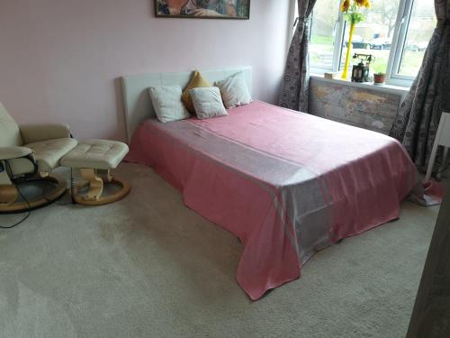 a bedroom with a pink bed with a chair and a window at Beautiful Apartment in High Wycombe in Buckinghamshire