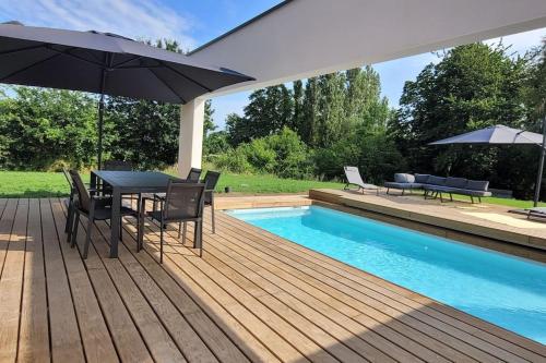 - une terrasse en bois avec une table et un parasol à côté de la piscine dans l'établissement Villa neuve contemporaine avec piscine, à Fouesnant