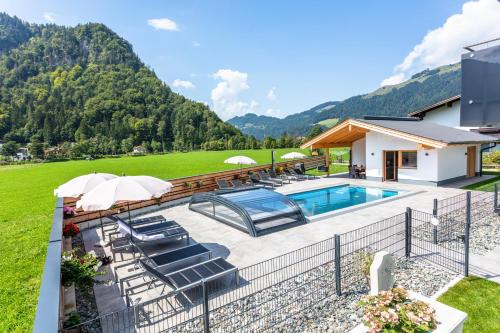 a swimming pool with chairs and umbrellas next to a house at Kaiser Apart Walchsee in Walchsee