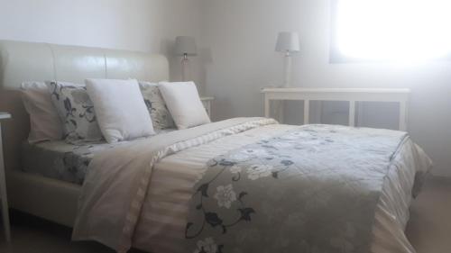 a white bedroom with a bed with a blanket and pillows at Haatsmaout City center apartment Ashdod in Ashdod