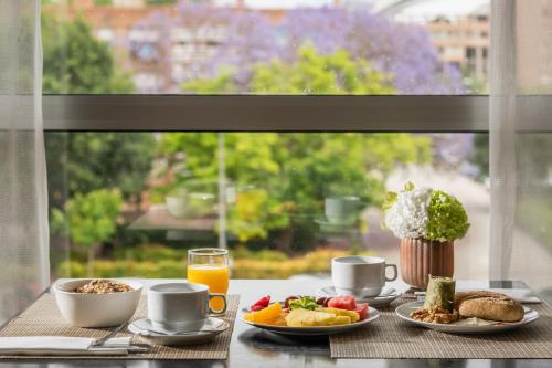 Una mesa de desayuno con alimentos para desayunar y jugo de naranja y una ventana. en Hotel Medium Valencia, en Valencia