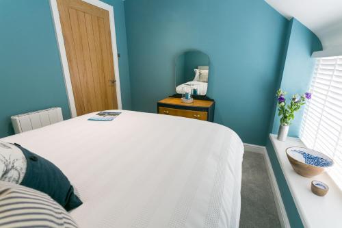 a bedroom with a white bed and blue walls at Cae Coch in Newborough