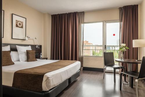 バレンシアにあるホテル ミディアム バレンシアのベッド、デスク、窓が備わるホテルルームです。