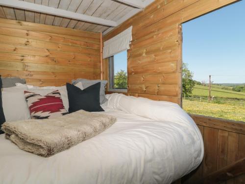 a large bed in a wooden cabin with a window at The Snug in Dulverton