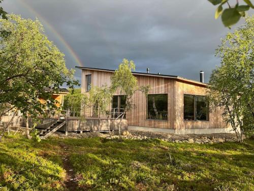 een houten huis met een regenboog op de achtergrond bij Villa Aitti in Utsjoki