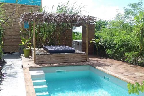 a swimming pool with a bench and a bed next to a swimming pool at LE TIKI gîte côté canne in Grand-Bourg