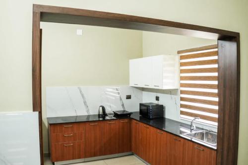 Zennova Furnished Apartment في أليبي: مطبخ بدولاب خشبي ومغسلة وميكروويف