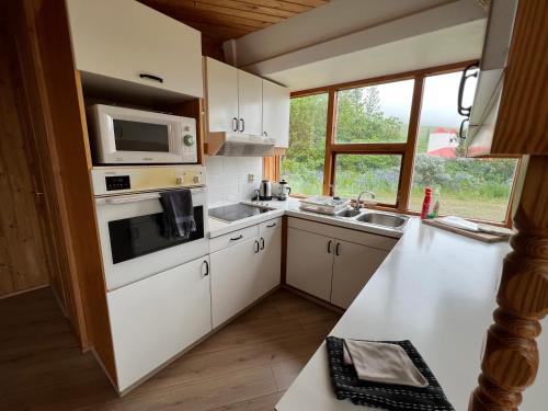 a kitchen with white cabinets and a microwave and a sink at Apartment dome Hof í Vatnsdal in Blönduós