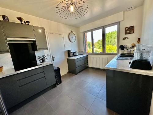 une grande cuisine avec des armoires noires et une horloge au plafond dans l'établissement La demeure des vents, au Tilleul