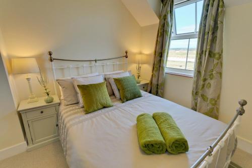 a bedroom with a bed with green pillows and a window at Penrhyn Gwyn in Aberffraw