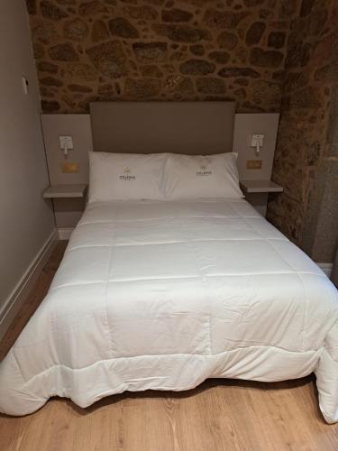 Una cama con sábanas blancas y almohadas en un dormitorio en hostal Hcelenis, en Caldas de Reis
