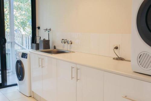 een witte keuken met een wastafel en een wasmachine bij Cheerful family home with stunning views in Caloundra
