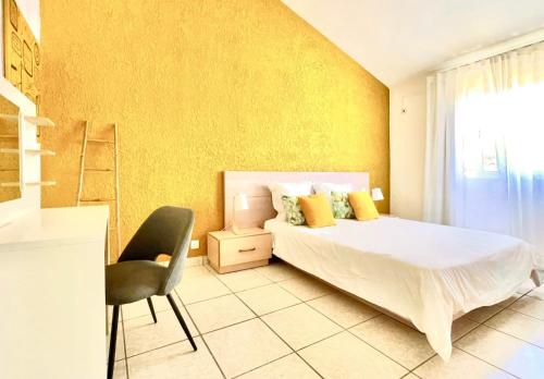 1 dormitorio con cama, silla y pared amarilla en Azur - Résidence Le Dattier, en Flic en Flac