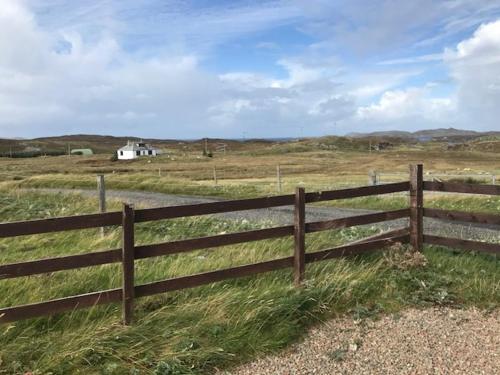 a wooden fence in a field with a house in the background at Harsgeir View Holiday Cottage -Wifi Go green in Breaclete