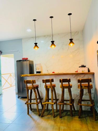 a kitchen with a bar with four wooden stools at Portuá Chalés in São Miguel dos Milagres