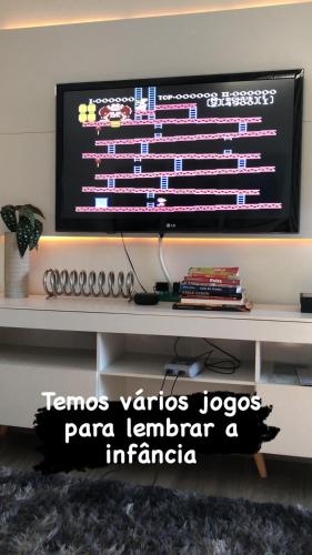 a television on a wall with a table with books at Uai House com jacuzzi, teto rooftop retrátil e colchão massageador in Poços de Caldas