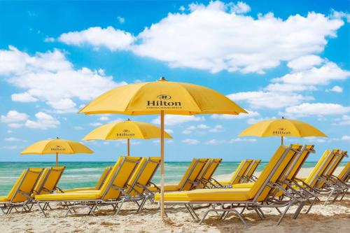eine Gruppe gelber Stühle und Sonnenschirme am Strand in der Unterkunft Hilton Cabana Miami Beach Resort in Miami Beach