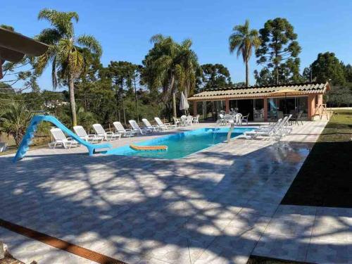 einem Pool mit Stühlen und einer Rutsche vor einem Haus in der Unterkunft CHÁCARA C/ PISCINA, SALÃO DE FESTA E CHURRASQUEIRA in Campo Largo