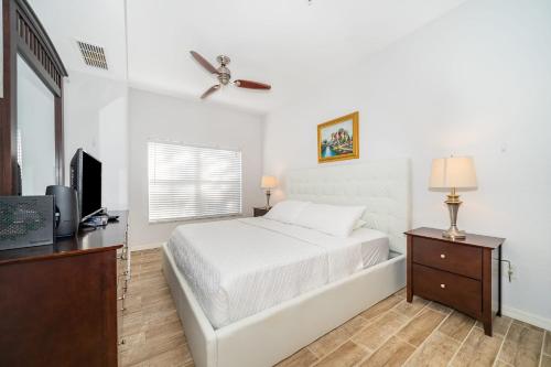 a white bedroom with a bed and a television at Enchanted Townhome near Disney Parks 3Br in Kissimmee