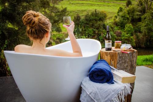 a woman sitting in a bath tub holding a wine glass at Ripples Retreat - Riverside in Piopio